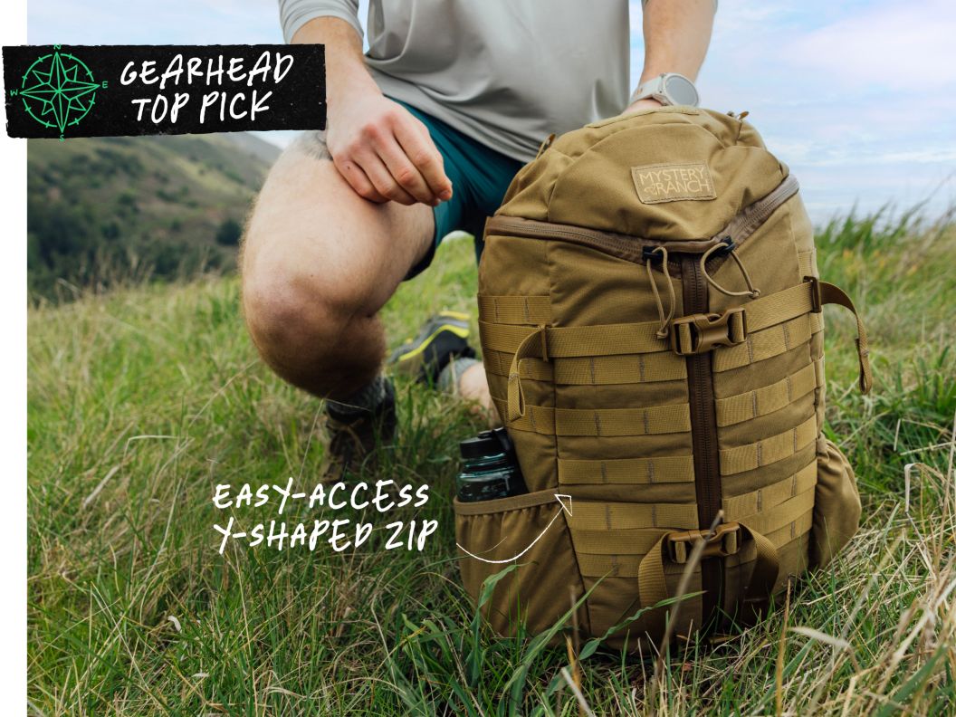 A man kneels in a meadow with a tan backpack. Text overlay reads: gearhead top pick easy-access Y-shaped zip.